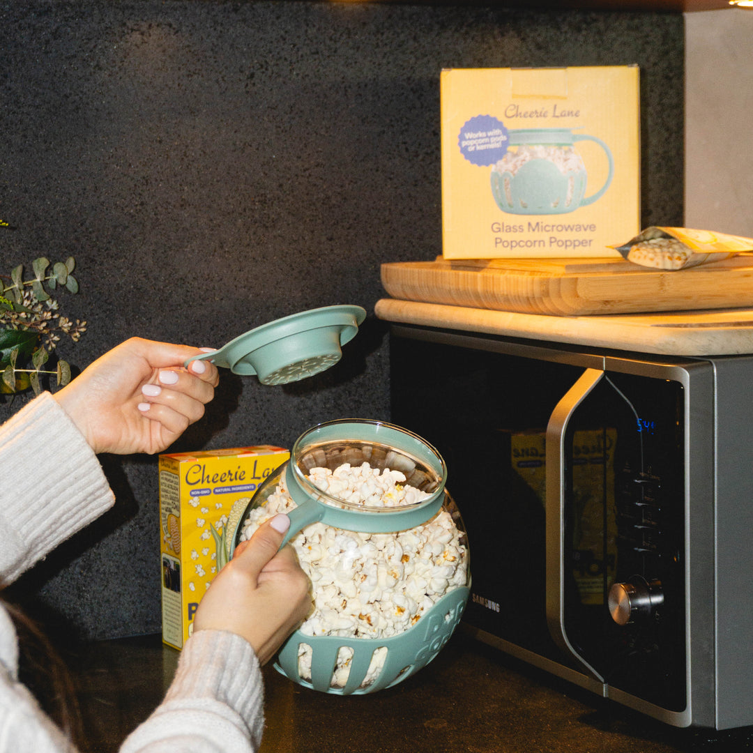 Person making popcorn using a microwave and ingredients on a kitchen counter.
