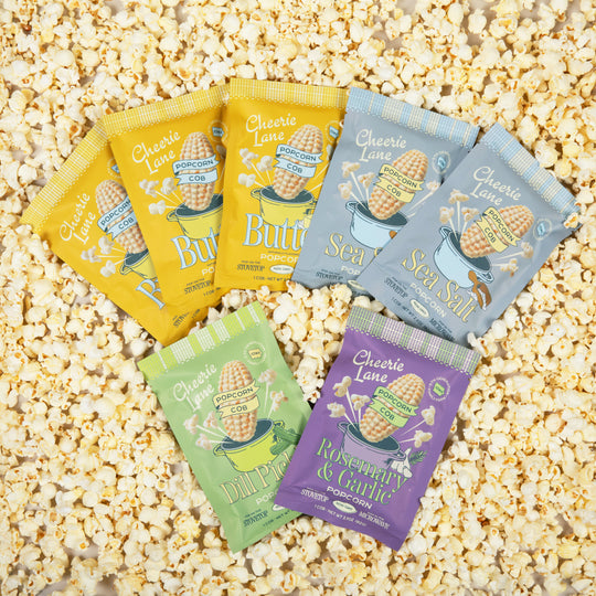 Assorted Cheerie Lane popcorn packages on a bed of popcorn kernels.