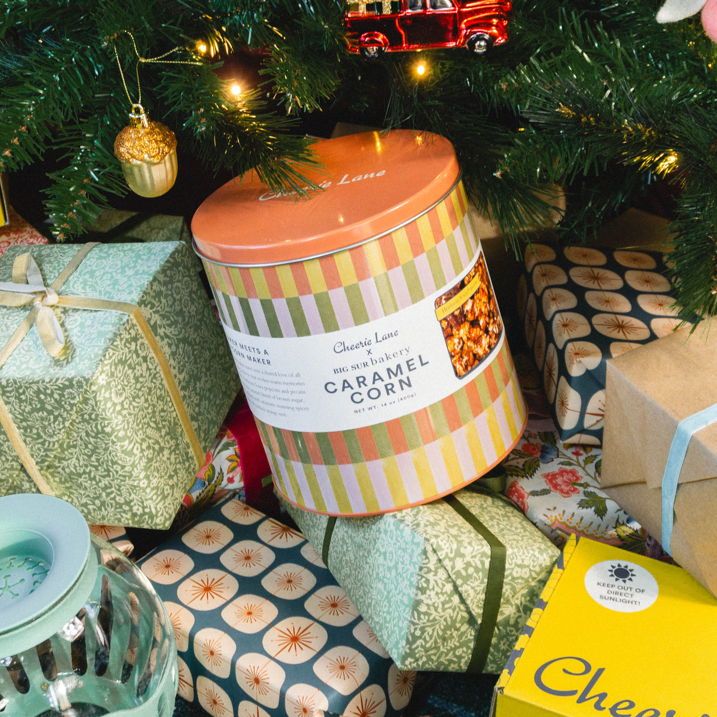 Caramel corn gift box under a Christmas tree with presents and decorations.