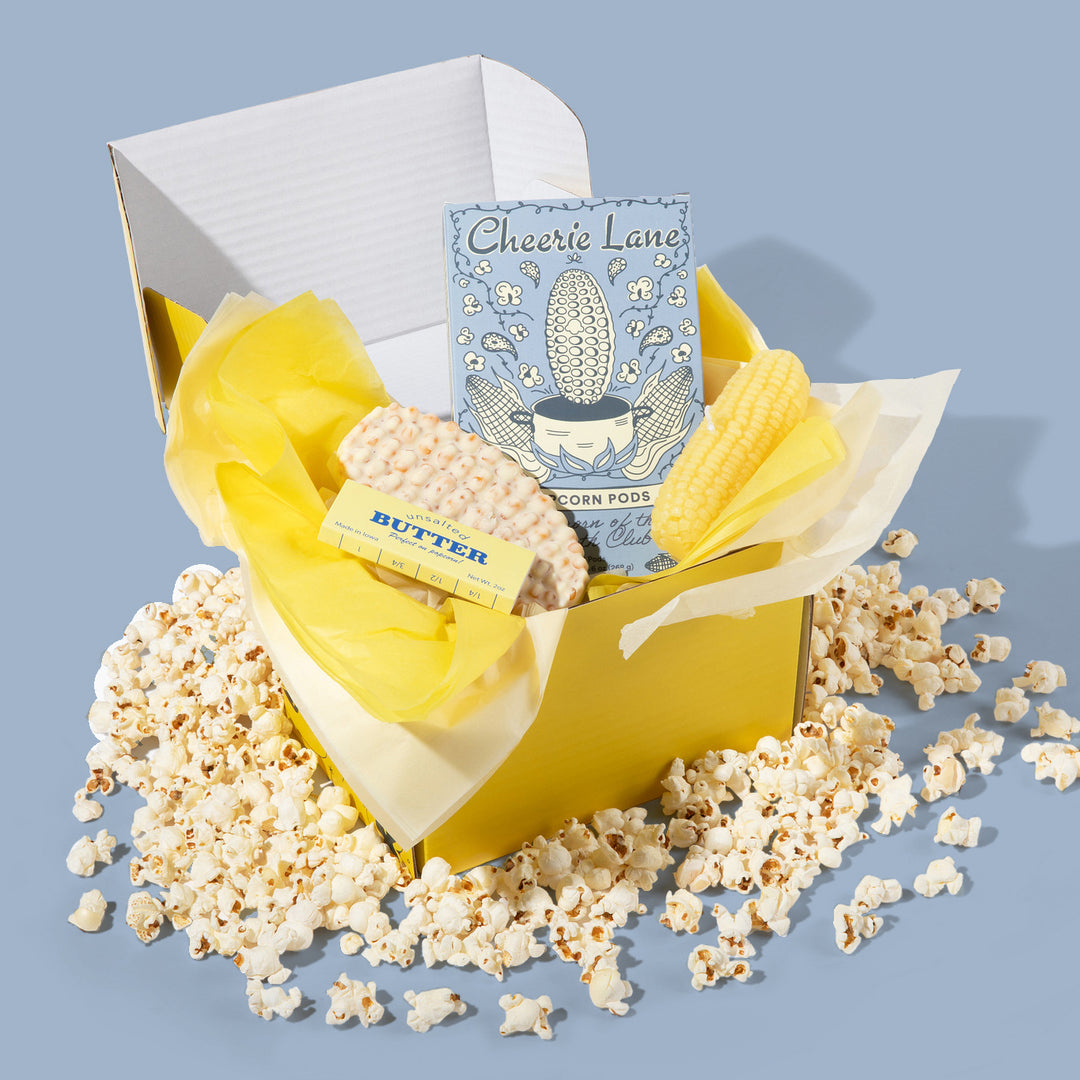 Yellow gift box with popcorn, corn pods, and a card on a blue background